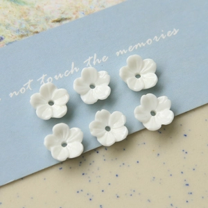 Détail de six perles fleurs en résine blanche avec trous centraux sur fond bleu