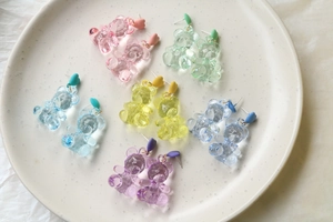 Macro detail of colorful resin gummy bear earrings on a light ceramic texture tray