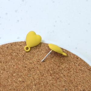 Close-up of matte yellow heart earring studs with metal needles on cork surface