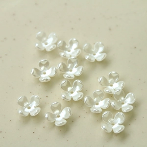 Macro shot of 12 white pearl-like acrylic four-leaf flower beads with center holes