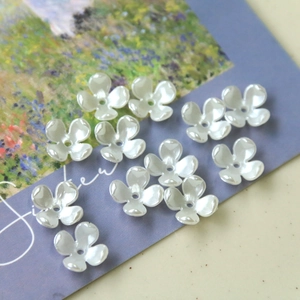 Detail showing pearlescent white four-petal flower charms with center holes for DIY crafts