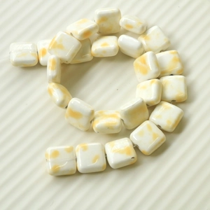 Detail of square ceramic beads with yellow cow print pattern on wavy display board