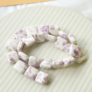 Close-up of square ceramic beads with purple cow print texture on a decorative white dish
