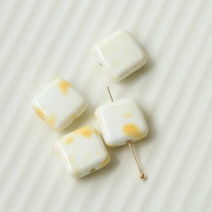 Close-up of square ceramic beads with yellow ink splash patterns for DIY jewelry making