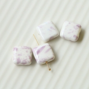 Macro view of square ceramic beads with purple ink splatters for handmade jewelry
