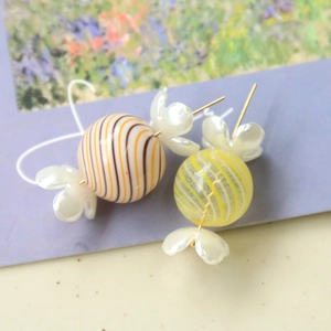 Detail of candy-shaped earrings with orange striped beads and white pearl petals