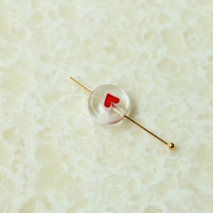Makro-Detail einer transparenten Glasperle mit rotem Herz auf einem Goldstift