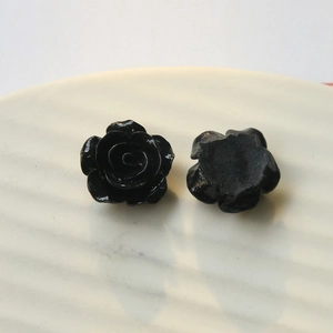 Detail of glossy black resin rose charms showing both front and flat back on ceramic tray