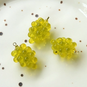 Dettaglio di tre ciondoli a forma di uva in resina verde con anelli dorati