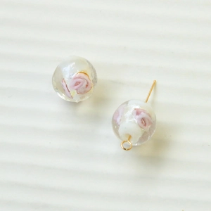 Detail einer handgefertigten Glasperle mit rosa Blumenmuster und goldener Metallschlaufe