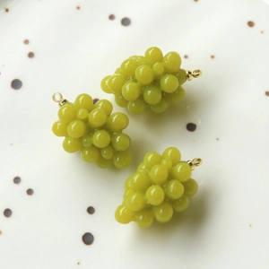 Dettaglio macro di tre ciondoli a uva in resina verde con ganci in metallo dorato