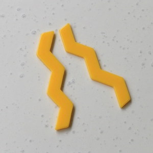 Vue macro de deux pièces de bijoux en acrylique jaune ondulé sur surface marbrée