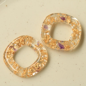 Dettaglio di pendenti quadrati in resina con foglia d'oro, petali e perle bianche