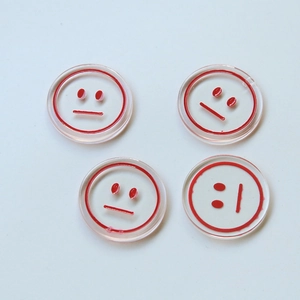 Detail of four transparent round resin charms with red smiley face prints for DIY jewelry