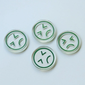 Detail of four transparent resin charms with green angry emoji prints for DIY jewelry