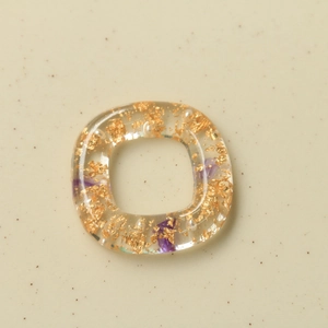 Vista macro di ciondolo in resina con foglia d'oro, petali viola e piccole perle bianche