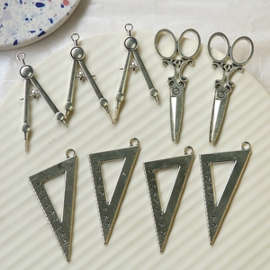 Macro detail of retro silver alloy charms set featuring compass scissors and triangle ruler