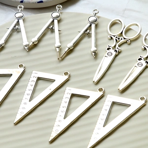Macro shot of vintage silver alloy charms featuring ruler, compass, and scissors designs