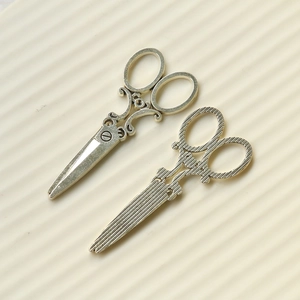 Detail of vintage silver scissor-shaped metal pendants with floral and striped textures