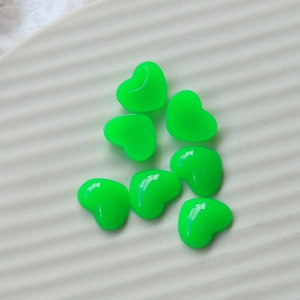 Macro detail of seven fluorescent green resin heart charms on a white textured ceramic dish