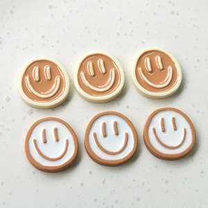 Close-up of cute round resin smiley face charms in brown and cream for DIY jewelry crafts