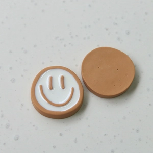 Detail showing the glossy white finish and brown smiley face on circular resin charms