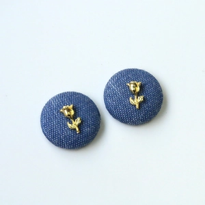 Detailed close-up of blue denim round buttons with golden rose metal relief accents