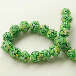 Macro detail of round glass beads with floral patterns in green, yellow, and white colors