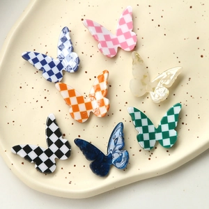 Flat lay of colorful checkerboard butterfly resin charms on a ceramic jewelry tray