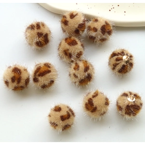 Macro detail of plush leopard print pom-poms with gold metal rings for DIY jewelry