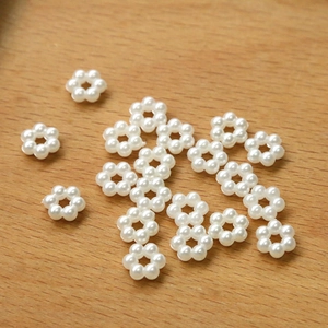 Macro shot of ivory floral faux pearl beads on a light wood grain surface for DIY jewelry