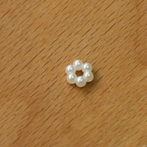 Macro shot of white acrylic pearl flower charm for DIY earrings on a wooden background