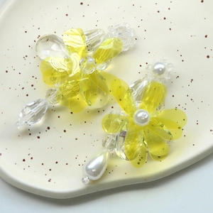 Detail of handmade yellow resin flower earring with clear beads and pearl drop on ceramic tray