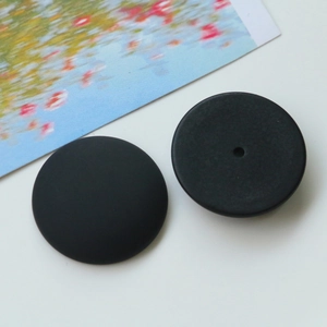 Macro detail of matte black resin charms showing front convex and back single-hole structure
