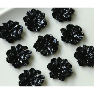 Flat lay of glossy black resin camellia flower charms for DIY jewelry and crafts