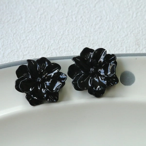 Detail of glossy black camellia flower studs on white ceramic plate with soft lighting