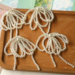 Detailed view of handmade pearl bow earrings with elegant fringe on a wooden tray