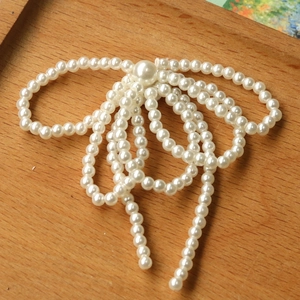Detail view of a handcrafted pearl bow ornament with flowing fringe on a wooden background