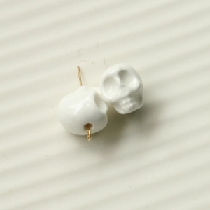 Close-up of white 3D skull resin charms with gold metal hooks for DIY jewelry making