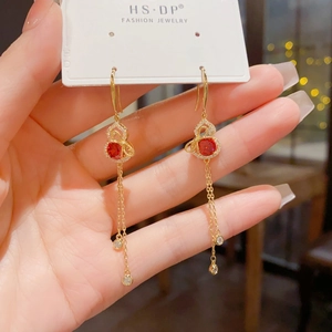 Close-up of golden gourd fringe earrings with red gemstone and sparkling zirconia