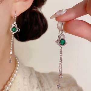 Close-up of dangling tassel earrings with emerald green gems and silver metal details