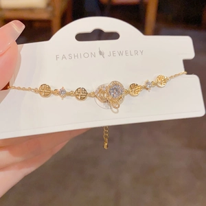 Détail du bracelet doré avec fleur en zircon et breloques de caractère Fu sur carte