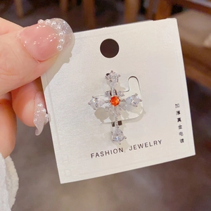 Detailed macro view of a crystal cross brooch with an orange centerpiece on display card