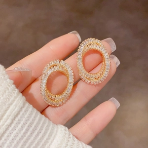 Détail de boucles d'oreilles ovales dorées avec zircons rectangulaires sur la main