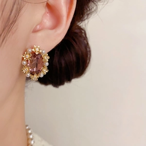 Detail of vintage flower earrings with oval purple gemstone and white pearls in gold finish