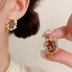 Detail of vintage flower earrings with purple crystal and small white pearls on gold metal