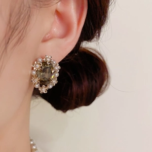 Detailed view of vintage gold flower earrings with olive green gems and pearls on model