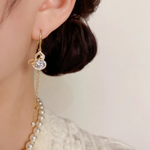 Détail de boucles d'oreilles gourde dorées avec zircons étincelants et fins pompons