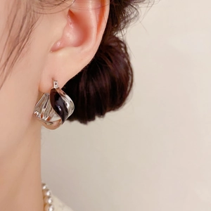 Close-up of a silver twisted earring with black enamel detail worn by a model
