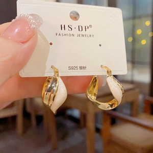 Close-up of golden metal twist earrings with cream enamel finish and S925 silver needle